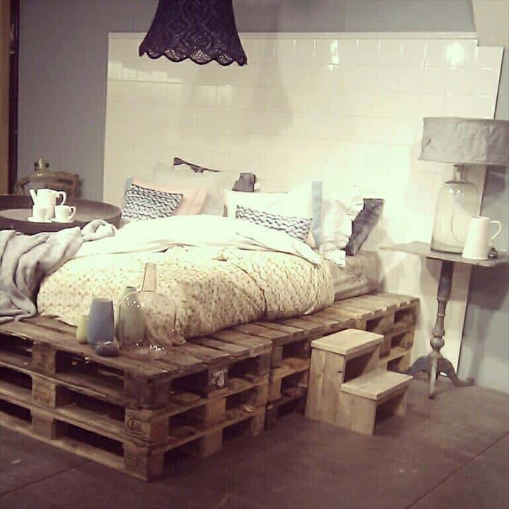 1. LAYERED PALLET FRAME BED WITH A WHITE TILE BACKGROUND SERVING AS A HEADBOARD