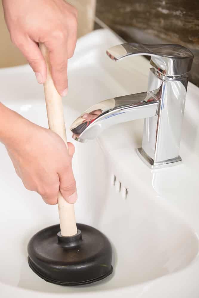 Plumber is cleaning sink with plunger.