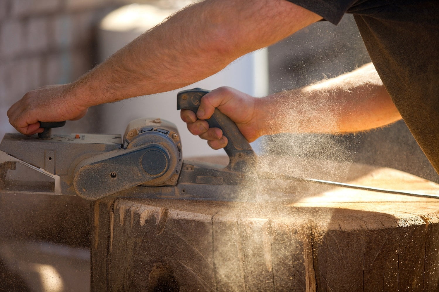 Carpenter working with an electric planer on a wooden STUMP in the open air. man treats wood plane. working joiner aligns the surface. carpenter's work