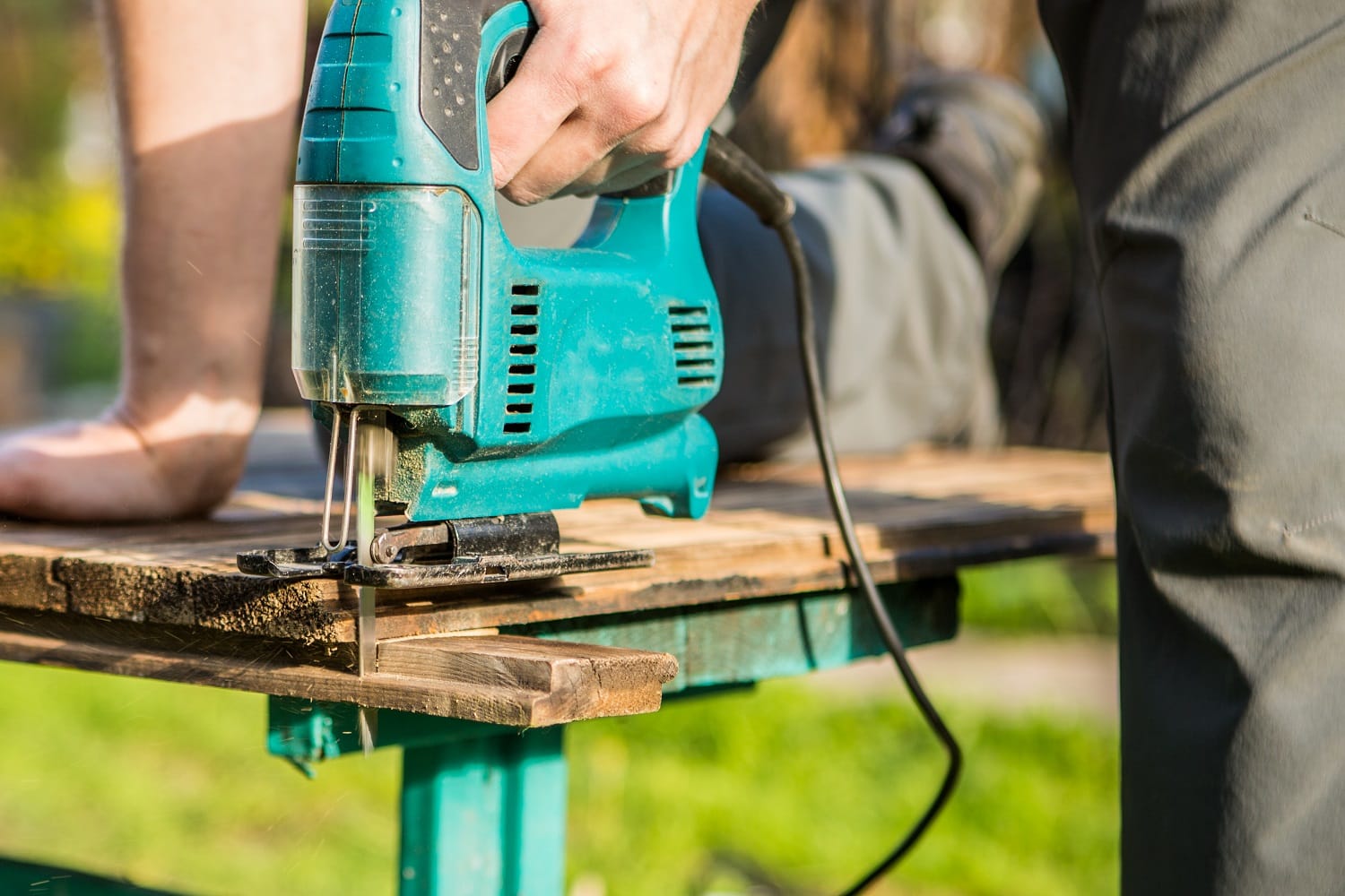 Photo of employee working with electric jigsaw in summer on street