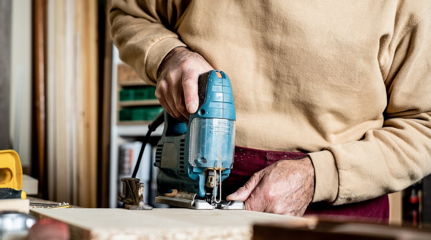 Carpenter's hands with electric jigsaw close-up. Work in a carpentry workshop. A man cuts plywood with an electric jigsaw. Electric tool for woodworking.