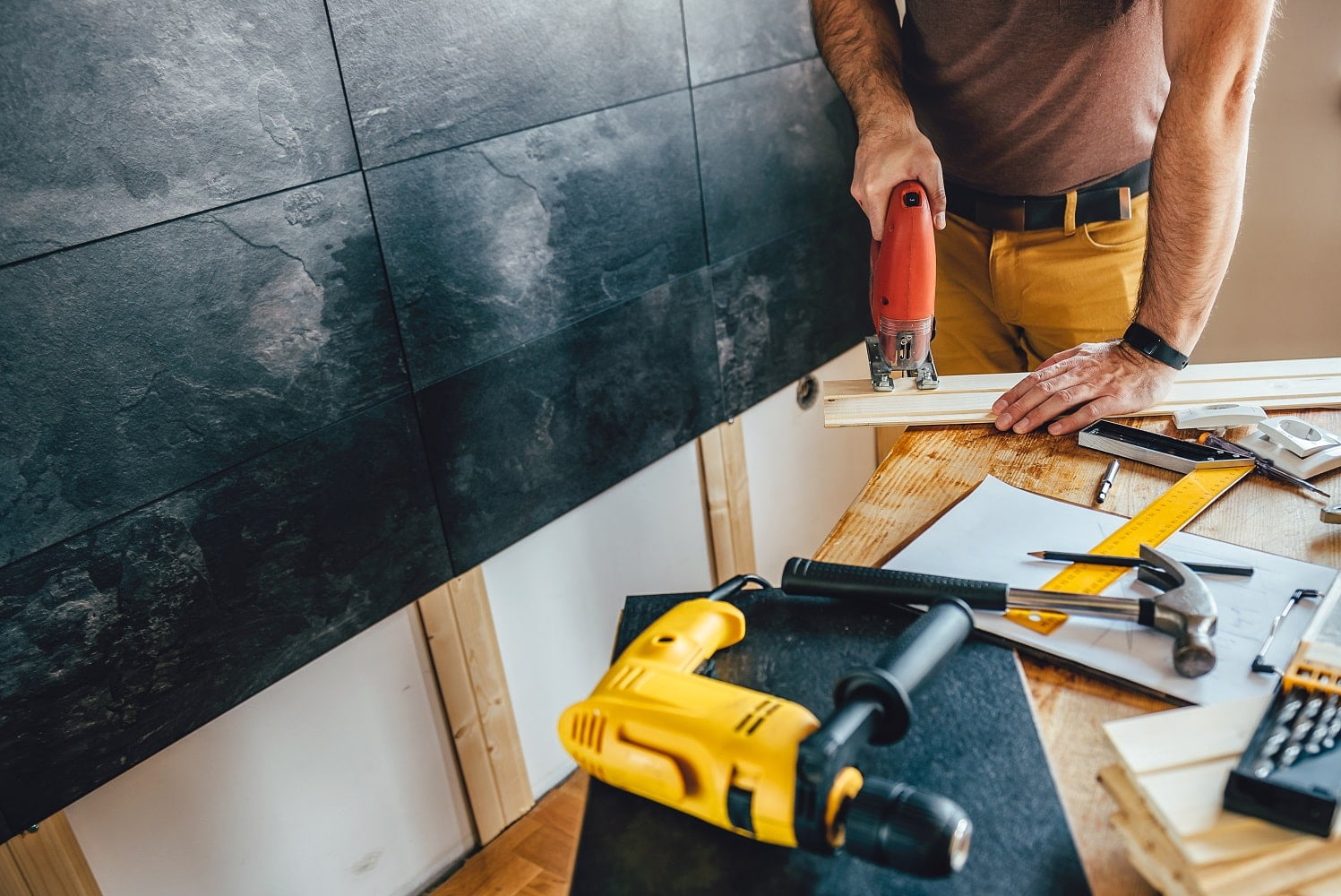 Man cutting piece of wood on the table with electric Jigsaw at home