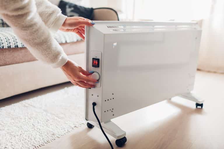 Using heater at home in winter. Woman regulating temperature on heater on wearing warm clothes. Heating season.