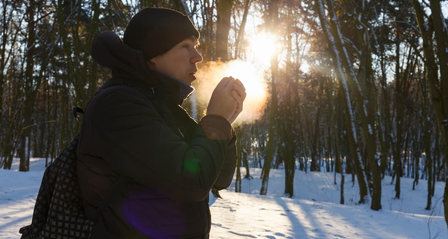 Young man warming up hands in snow covered forest