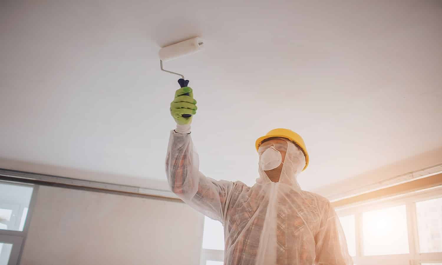 The builder works at the construction site and measures the ceiling. Worker with bucket and paint roller near wall. Best Bathroom Ceiling Paints Buyer’s Guide