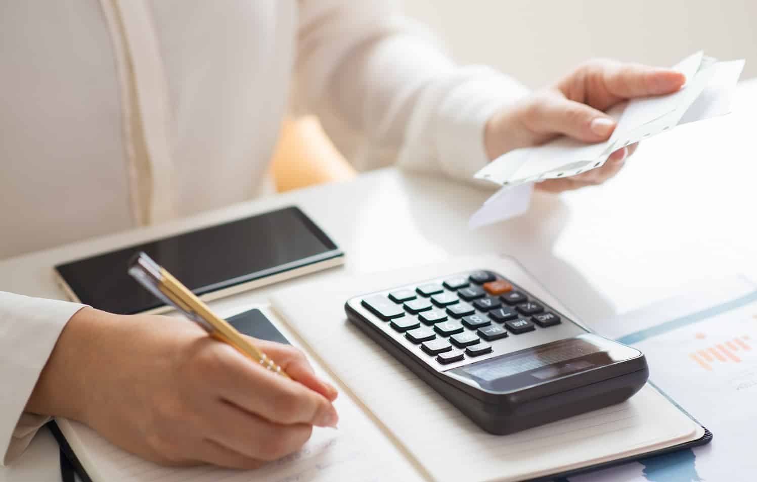 Closeup of person holding bills and calculating them. Notebook, calculator and smartphone lying on desk. Payment concept. Cropped view. Smart Pen Buyers’ Guide
