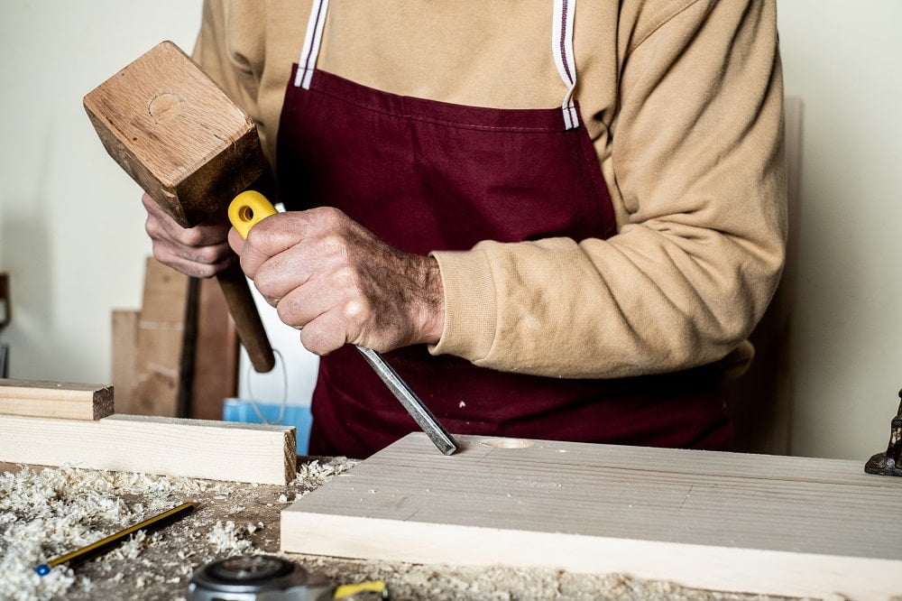 Carpenter's hands with chisel on the woodworking bench
