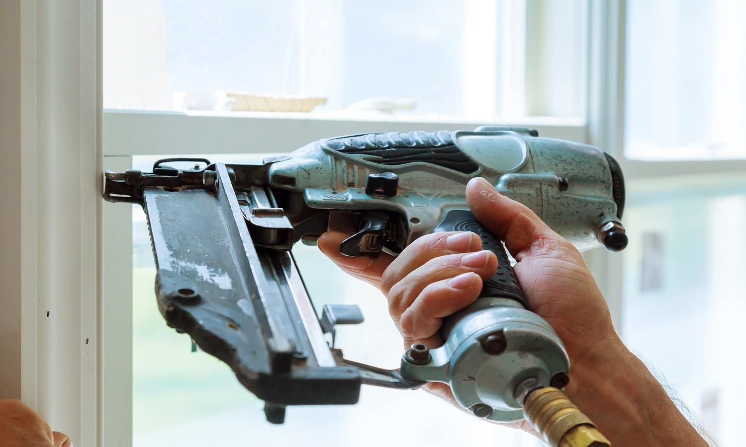 Carpenter brad using nail gun to moldings on windows, framing trim, with the warning label that all power tools have on them shown illustrating safety concept