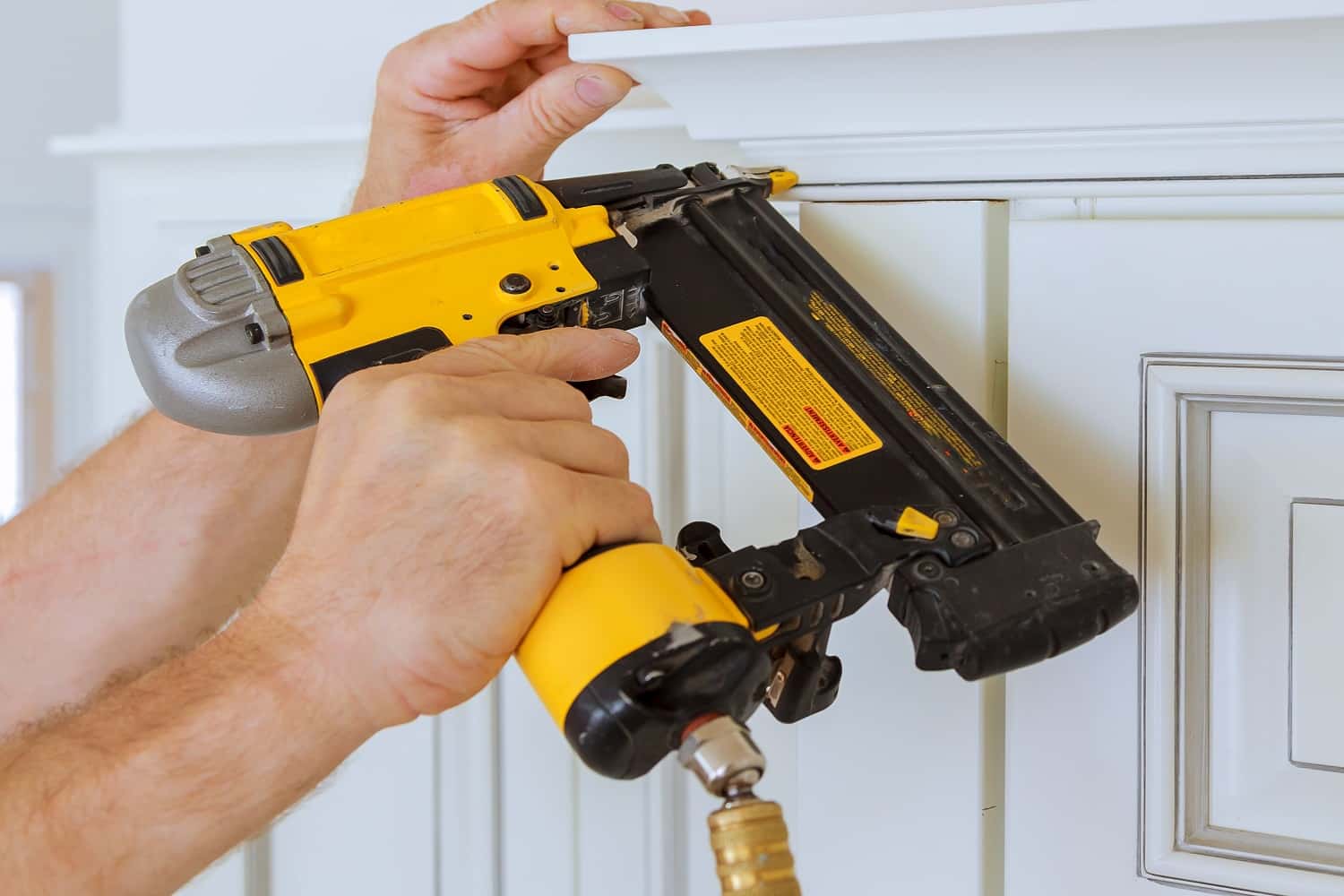Carpenter brad using nail gun to Crown Moulding on kitchen cabinets framing trim, with the warning label that all power tools have on them shown illustrating safety concept