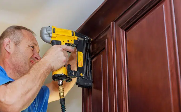 Carpenter brad using nail gun to Crown Moulding on kitchen cabinets framing trim, with the warning label that all power tools have on them shown illustrating safety concept