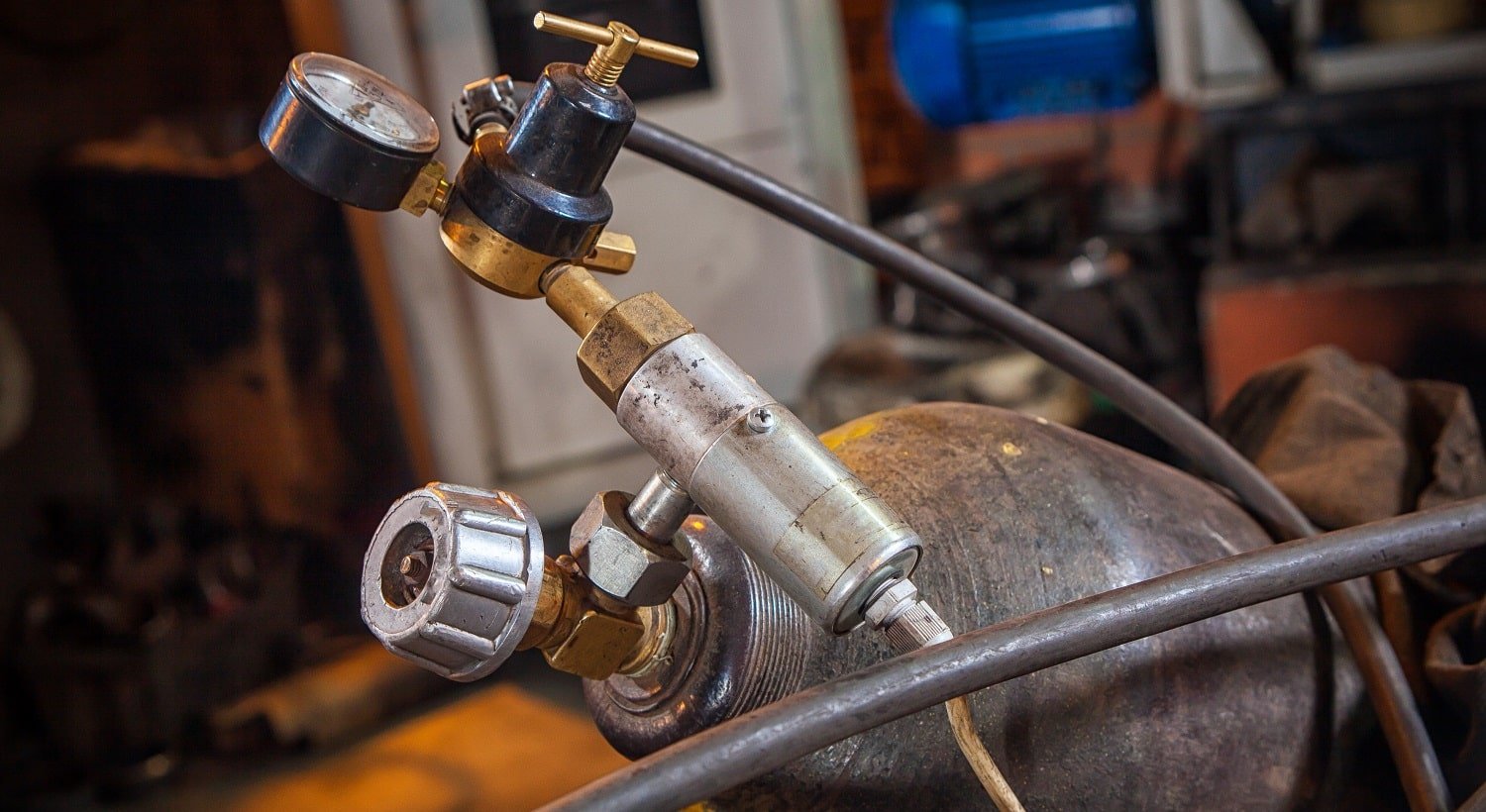 Close-up of a metal gas cylinder with a reducer and a pressure sensor in the background industrial workshop, side view