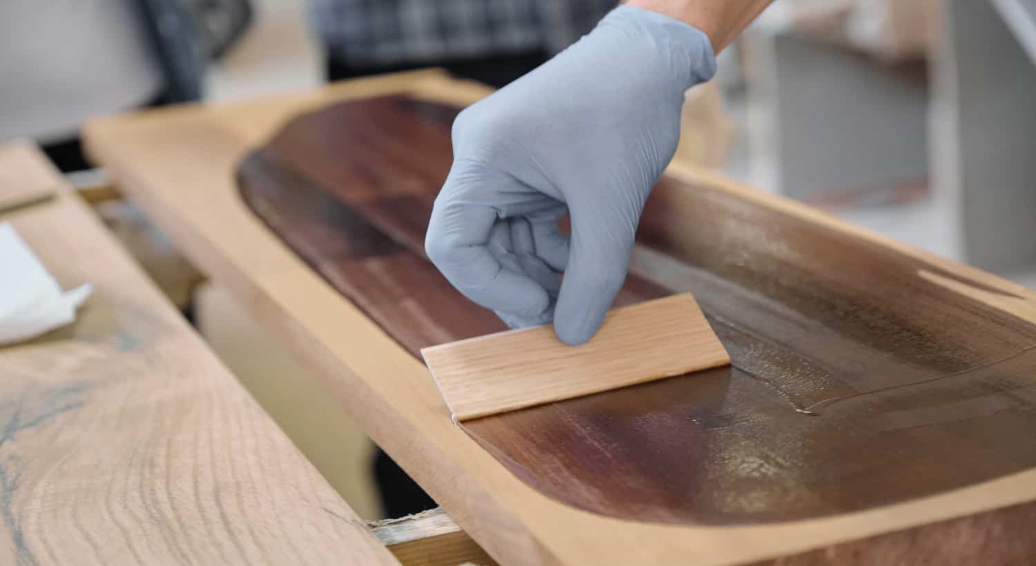 Closeup of workers hand covering wooden plank with finishing protective cover for wood, carpentry furniture woodworking production