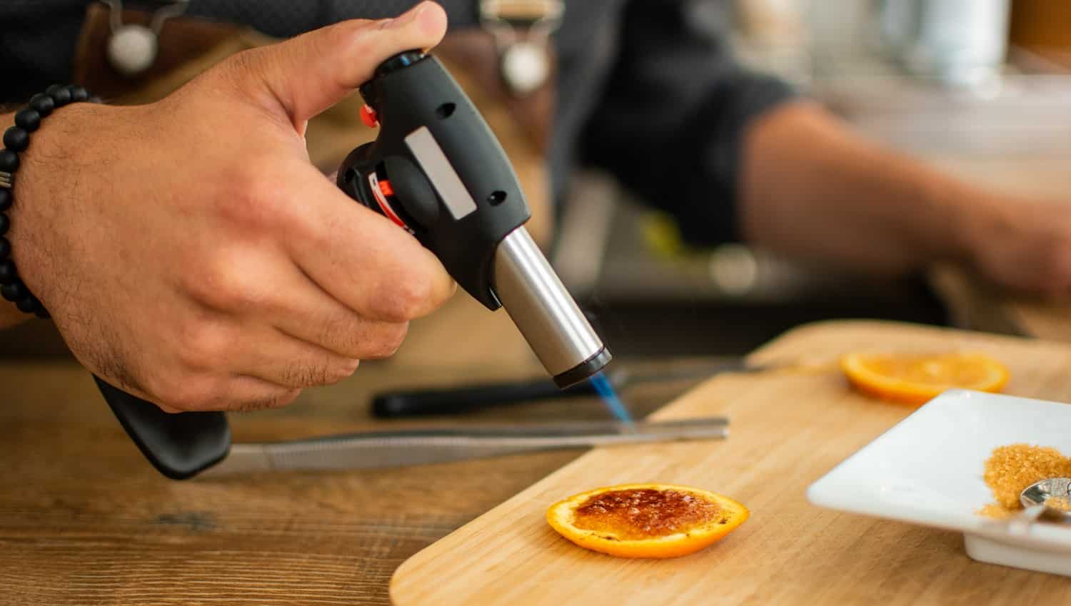 Barman burns orange with gas torch in bar for preparing cocktail. Profession concept.