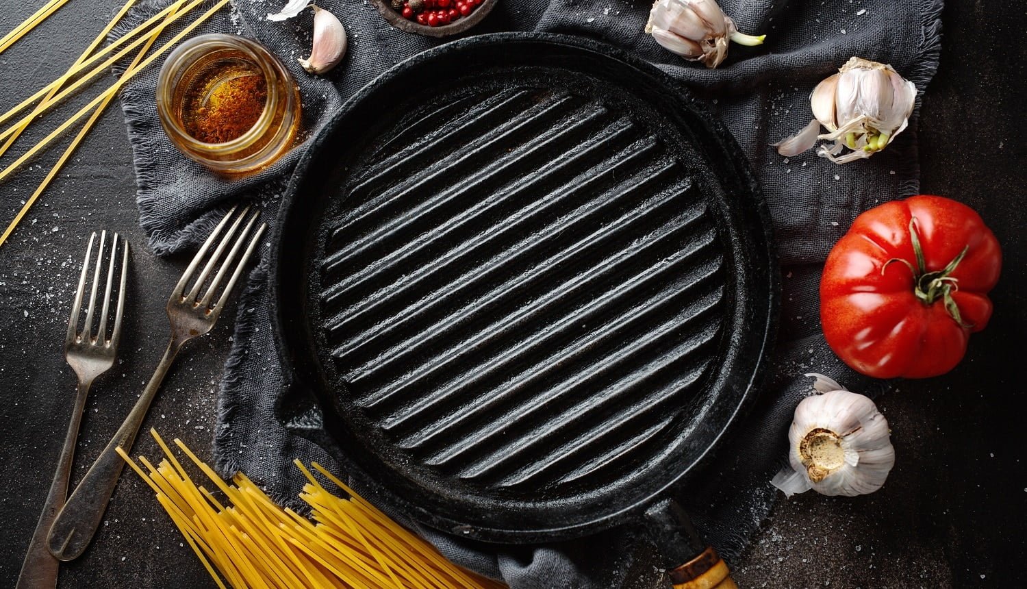 Italian food background with ingredients for cooking and grill pan on dark table.