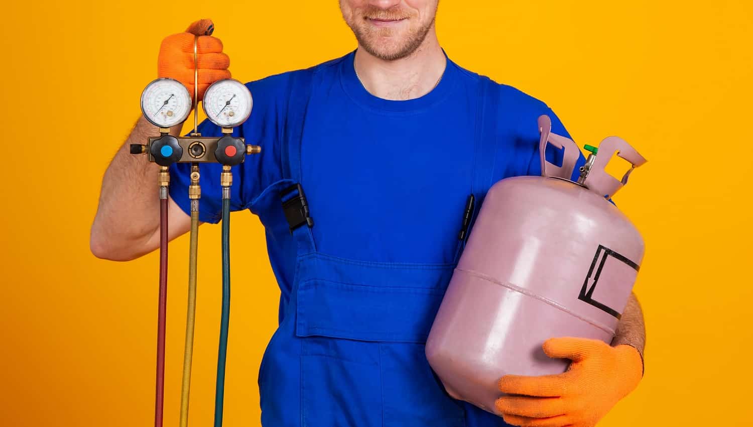 Young cheerful smiling air conditioning specialist. Repair of air conditioners and manometers, measuring equipment for refueling air conditioners. On a yellow background