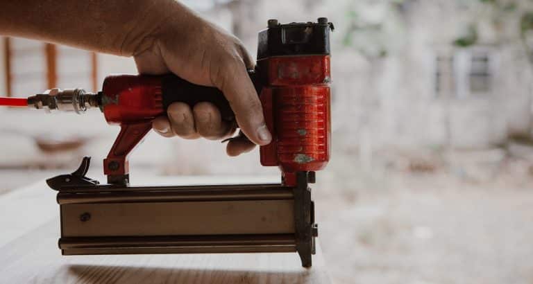 The carpenter is Making furniture the furniture .He is using a Staple gun to work.