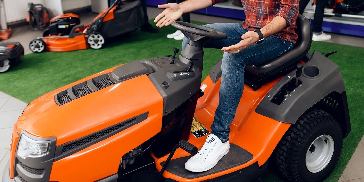 A man is sitting on a lawn mower in shop.