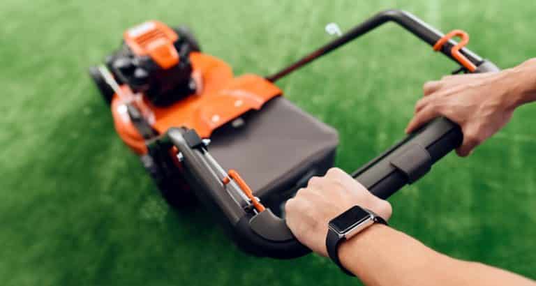 A man holds a lawn mower for the handle. Troy Bilt TB230