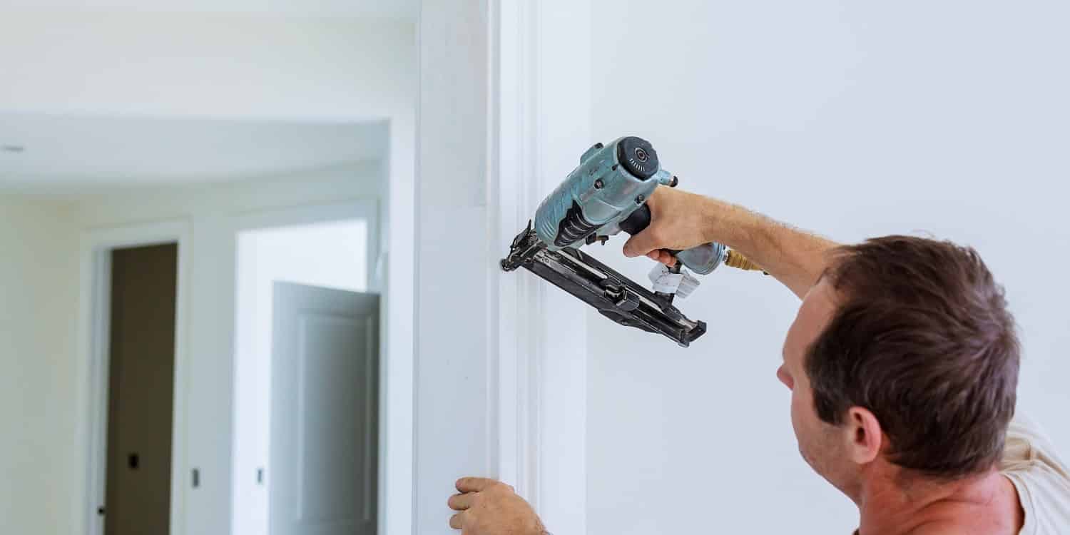 Carpenter brad using nail gun to moldings on doors, all power tools have on them shown illustrating safety concept