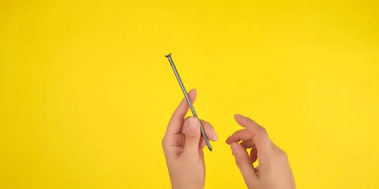 two female hands hold a large iron nail, yellow background, copy space