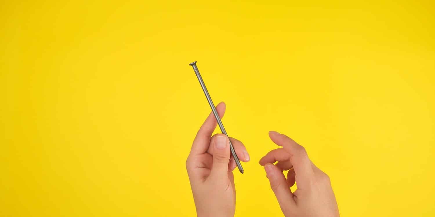 two female hands hold a large iron nail, yellow background, copy space