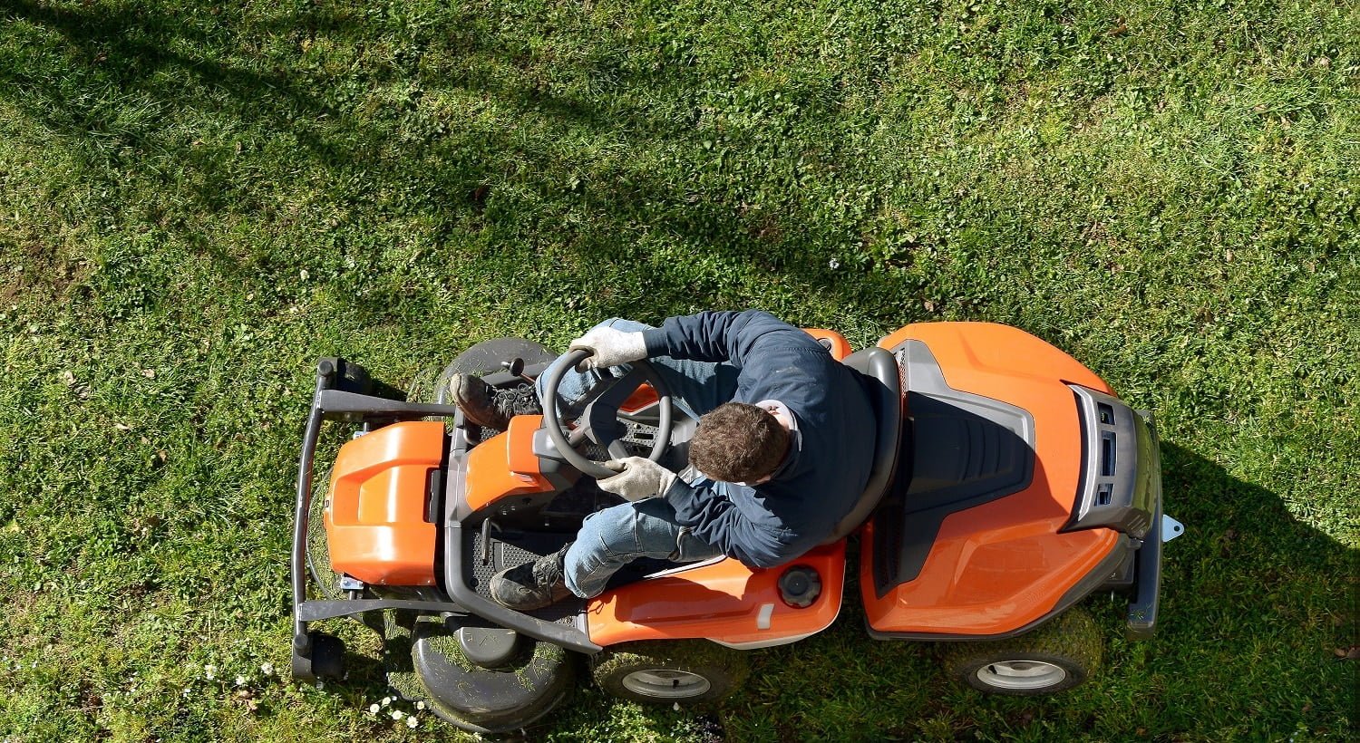 View from above of a man mowing a lawn on an orange ride-on mower as he attends to yard maintenance