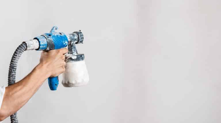 Worker painting wall with spray gun in white color.