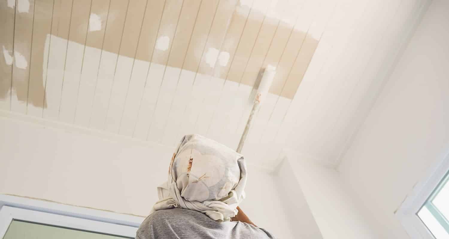 Partial focus photo of a man is painting ceiling using roller brush. Best Ceiling Paint