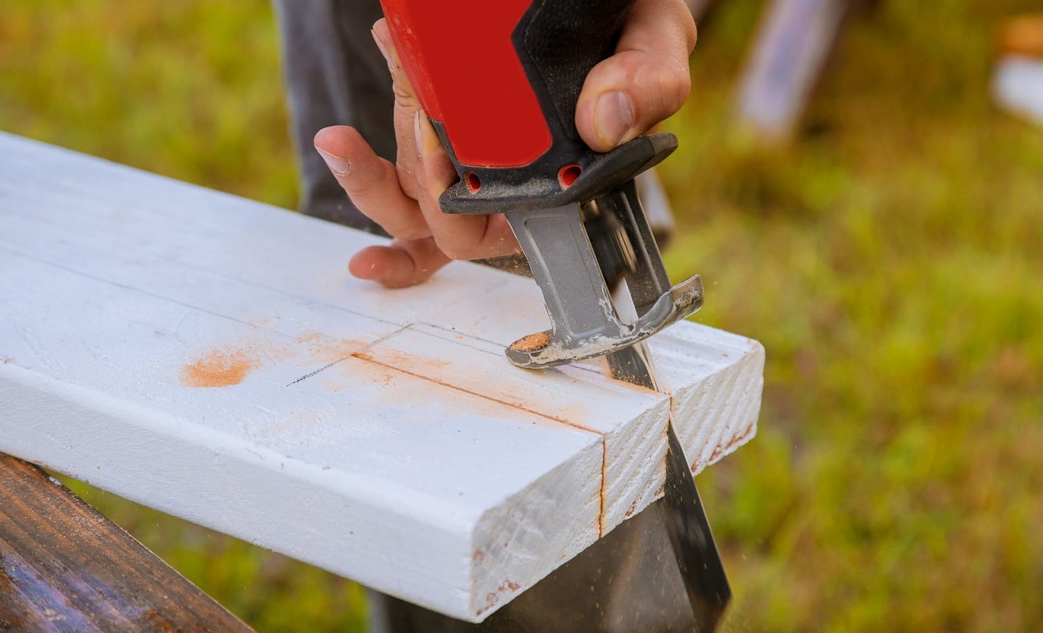 A man is cutting a board of wood with jigsaw detail of a cutting wooden board with saw dust.