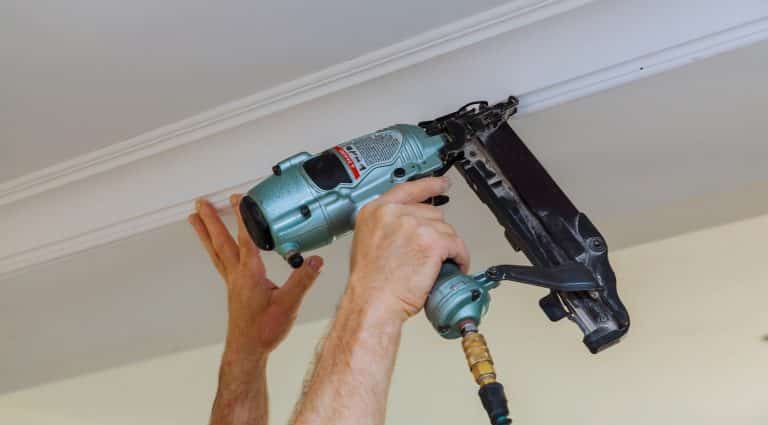 Carpenter brad using nail gun to Crown Moulding framing trim, with the warning label that all power tools have on them shown illustrating safety concept