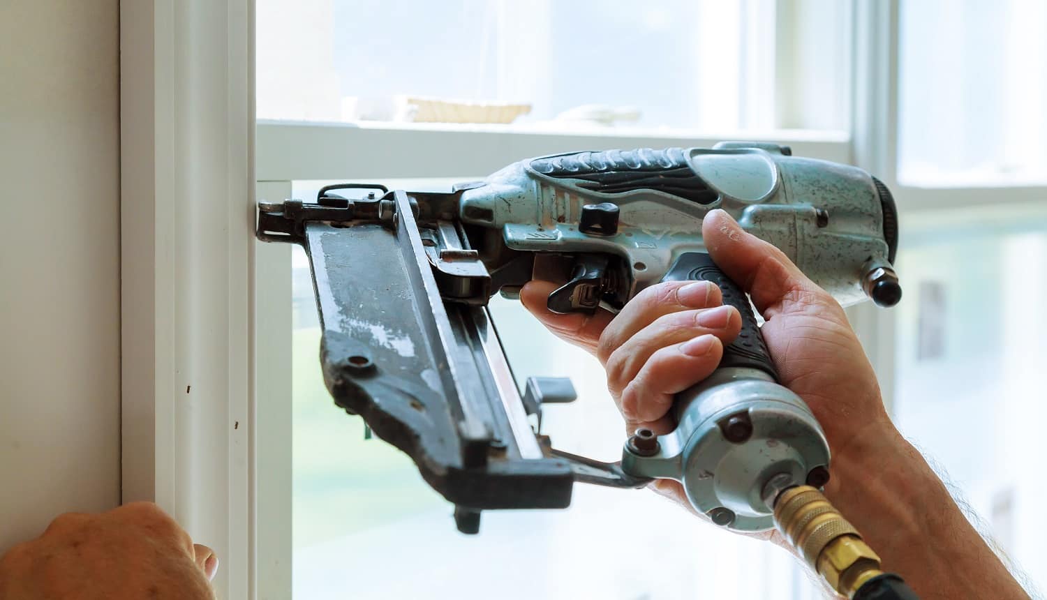 Carpenter brad using nail gun to moldings on windows, framing trim, with the warning label that all power tools have on them shown illustrating safety concept