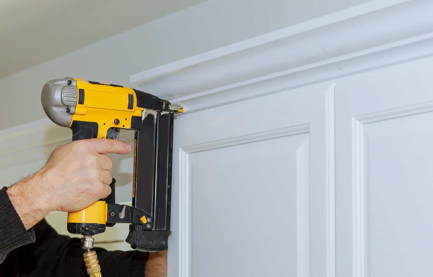 Handyman working using brad nail air gun to Crown Moulding on white kitchen wall cabinets framing trim, with the all power tools