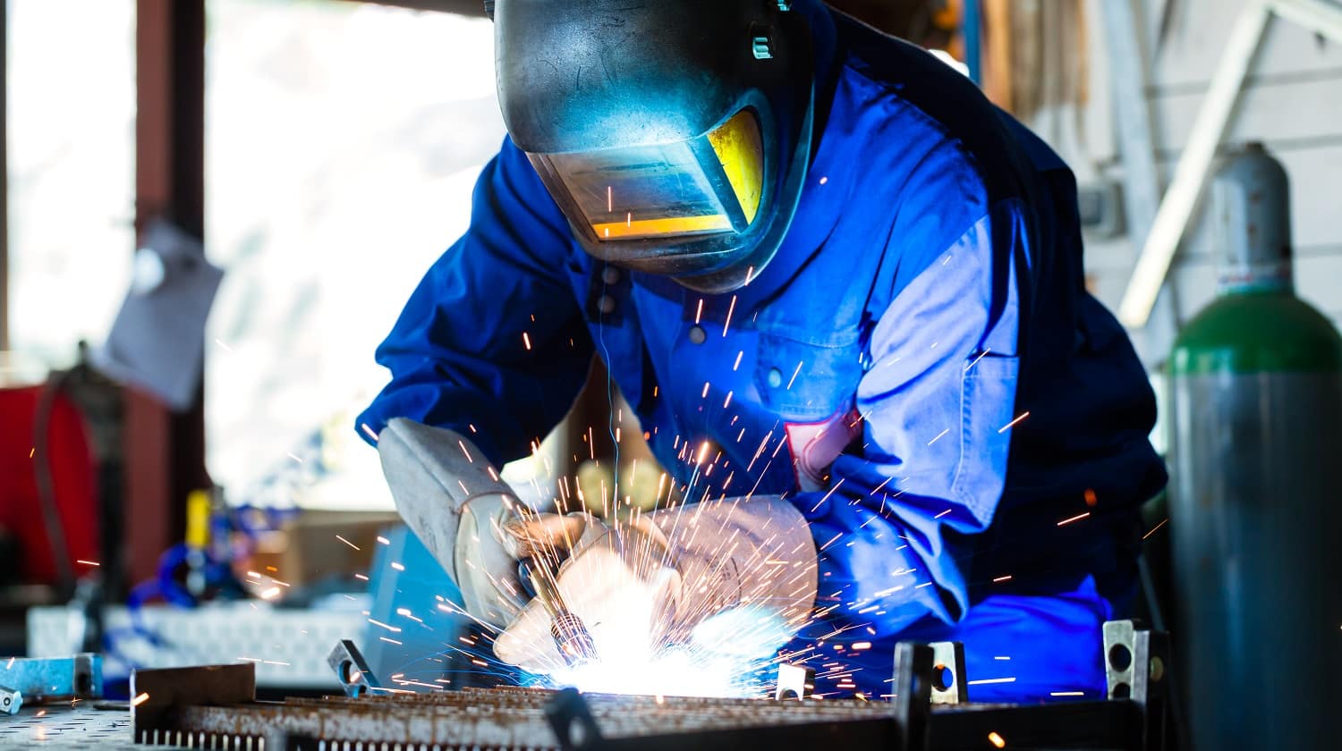 Welder bonding metal with welding device in workshop, lots of sparks to be seen, he wears welding googles