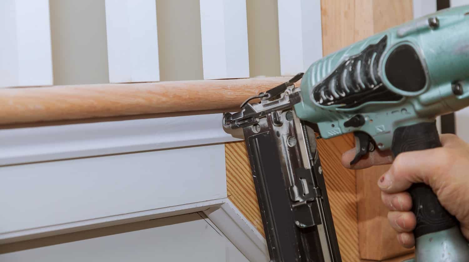 Carpenter brad using nail gun to Moulding trim, with the warning label that all power tools have on them shown illustrating safety concept. Freeman PFR2190 Review