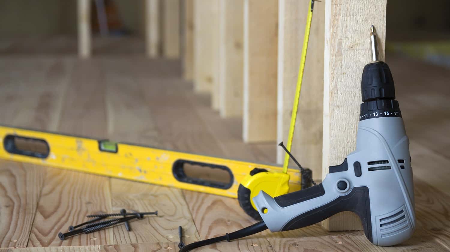 Close-up of professional tools: electrical screwdriver, level and measuring tape on background of wooden frame for future wall in attic room under reconstruction. Renovation and improvement concept.