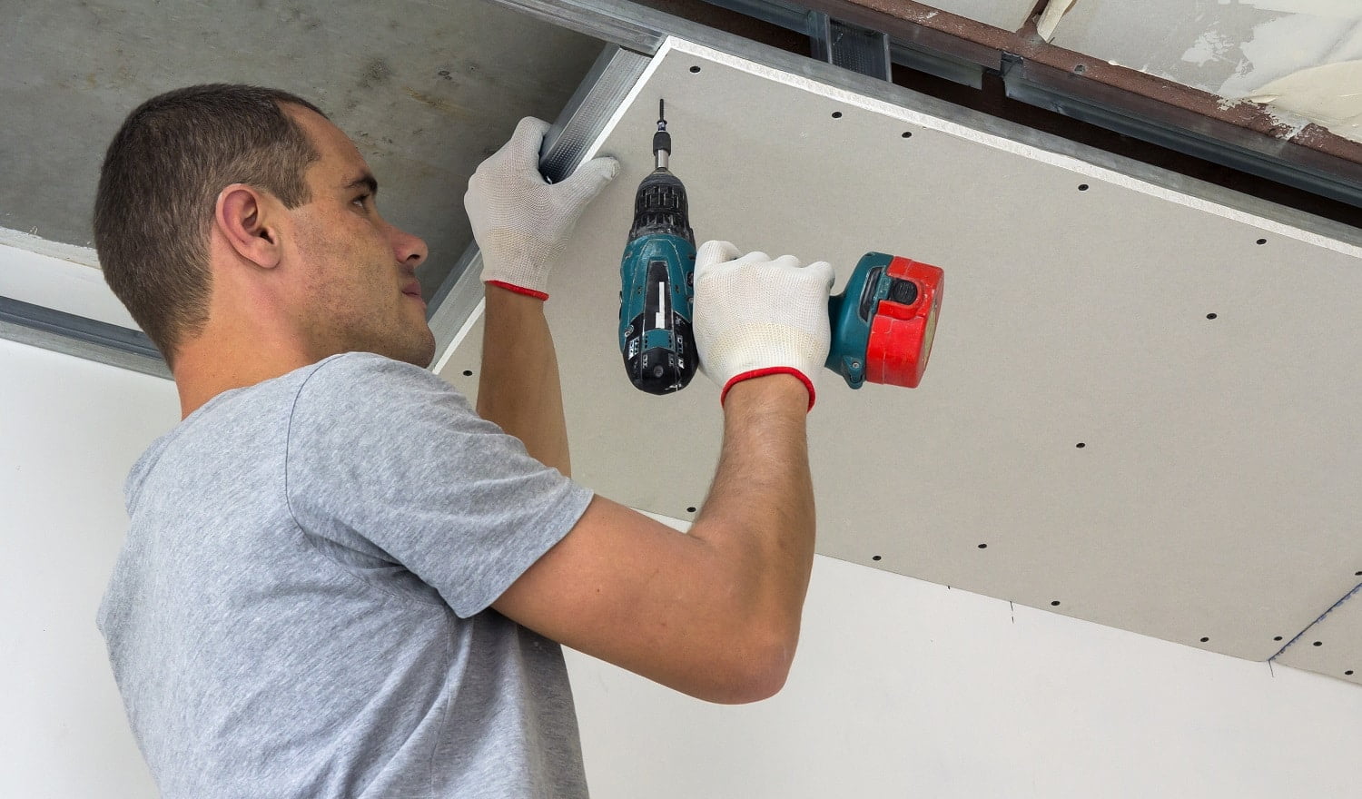 Construction worker assemble a suspended ceiling with drywall and fixing the drywall to the ceiling metal frame with screwdriver.