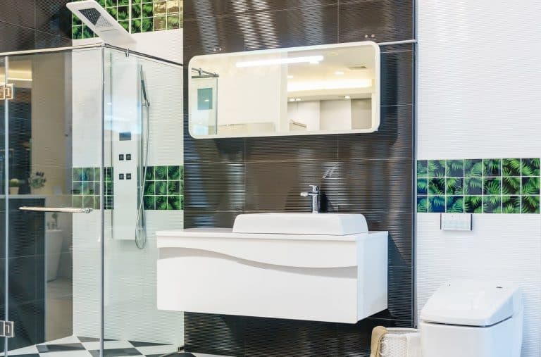 Spacious and bright modern bathroom interior with white walls, a shower cabin with glass wall, a toilet and faucet sink