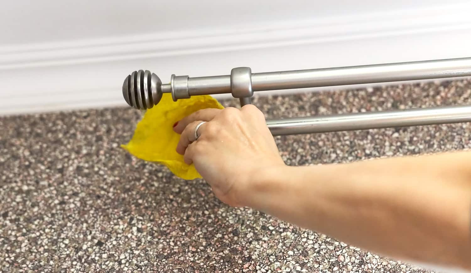 Woman washes a metal curtain rod with a yellow rag