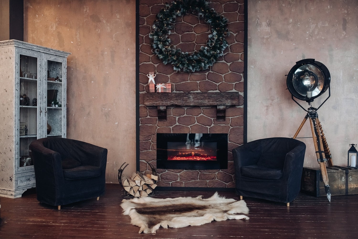 Christmas interior decorated with Christmas wreath made of fir branches. Two armchairs and a genuine animal fur on the floor in front of an electric fireplace.