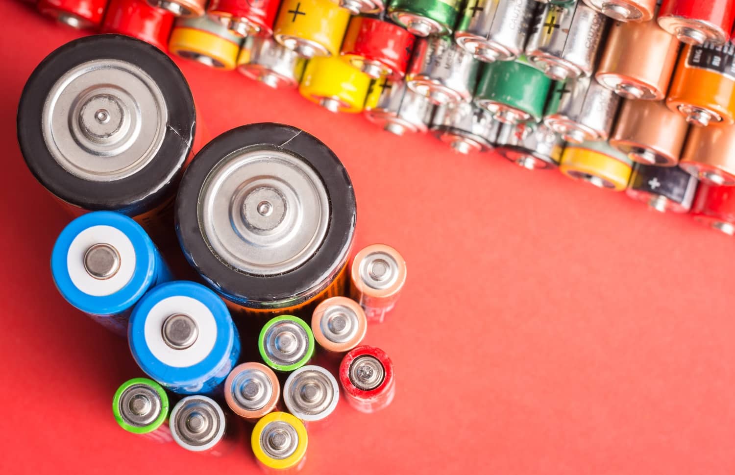 Batteries of different types and sizes on red background