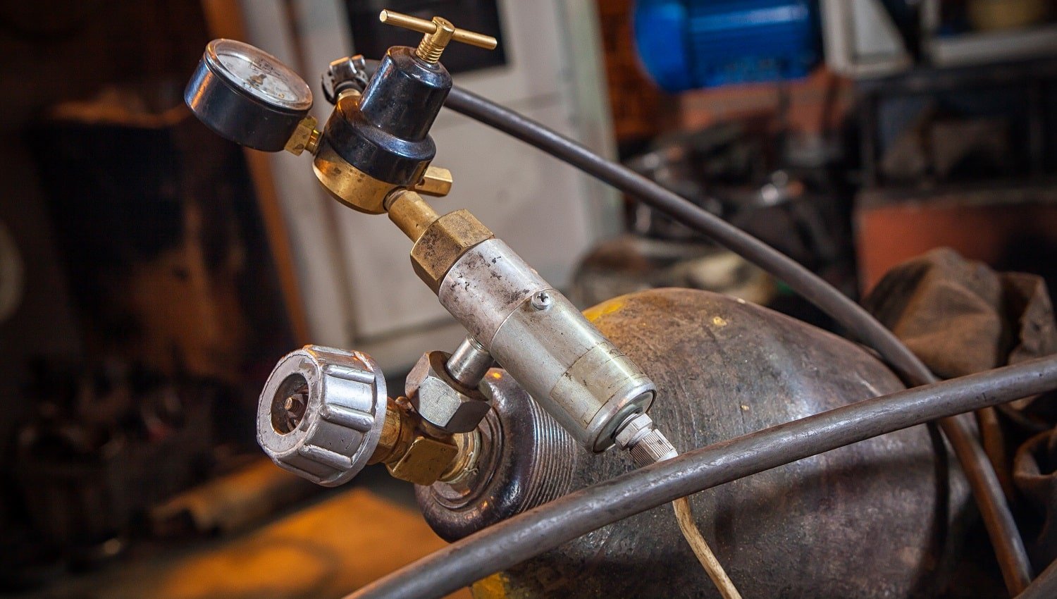 Close-up of a metal gas cylinder with a reducer and a pressure sensor in the background industrial workshop, side view