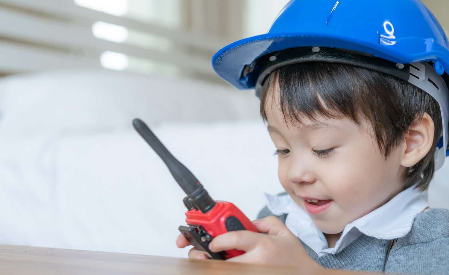 Little cute boy wearing blue helmet and enjoying to talking with red walkie-talkie redio in the bedroom