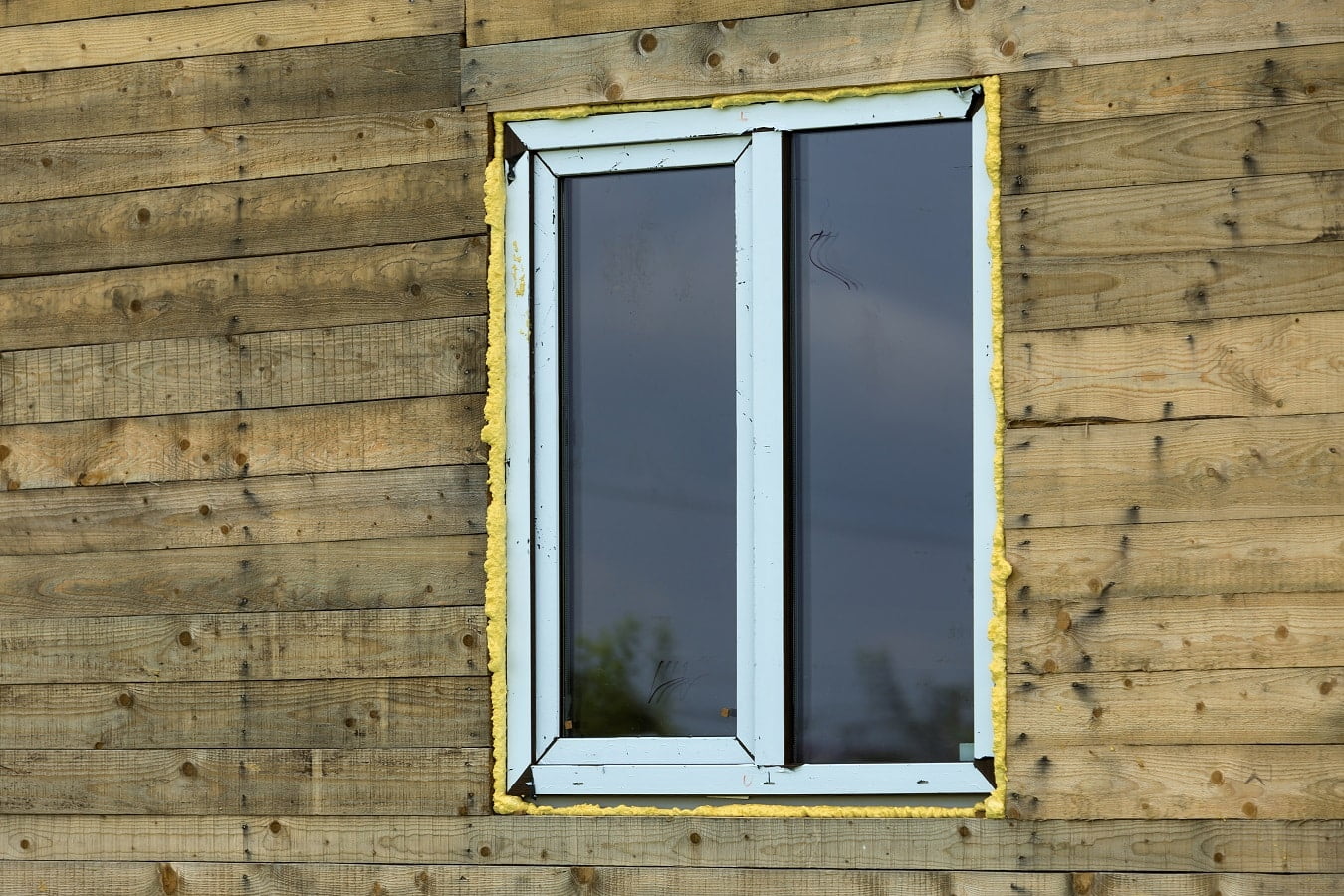 Close-up detail of new narrow plastic vinyl window installed in house wall of brown natural wooden planks and boards. Real estate property, comfortable cottage and professional construction concept.