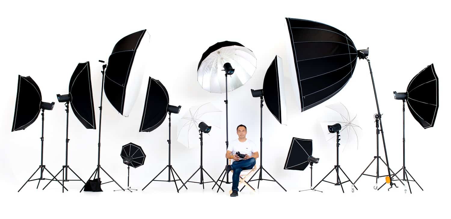 Asian photographers sit on the director's chair with flash studio lights a lot of patterns around on a white background.