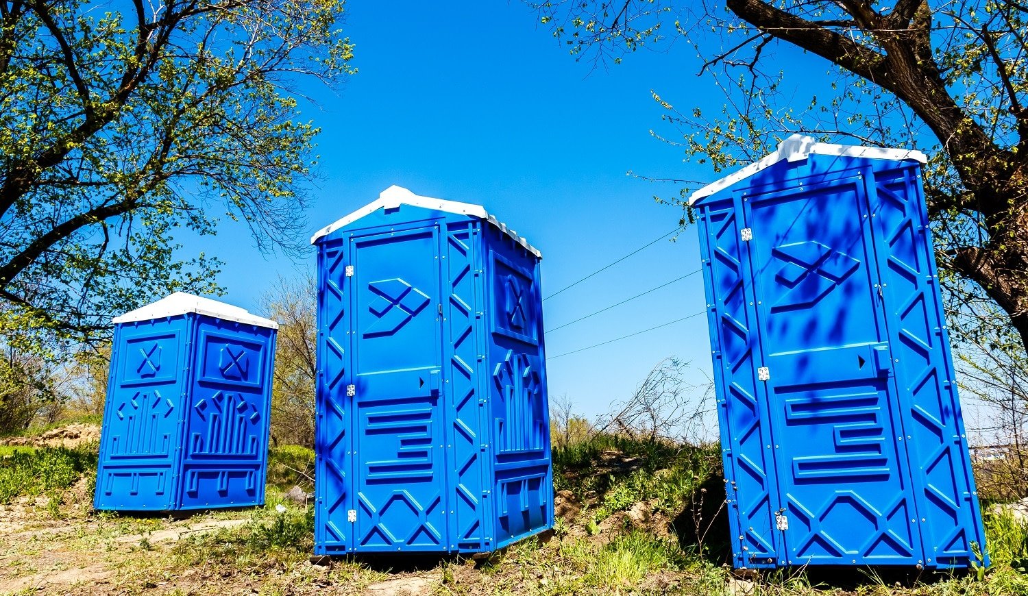 Three Blue Cabines Of Chemical Toilets In a Park at sunny Summer Day.