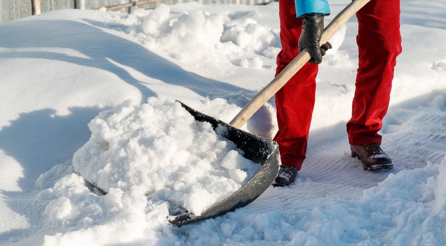 girl cleans snow shovel on the site near his house. sunlight day