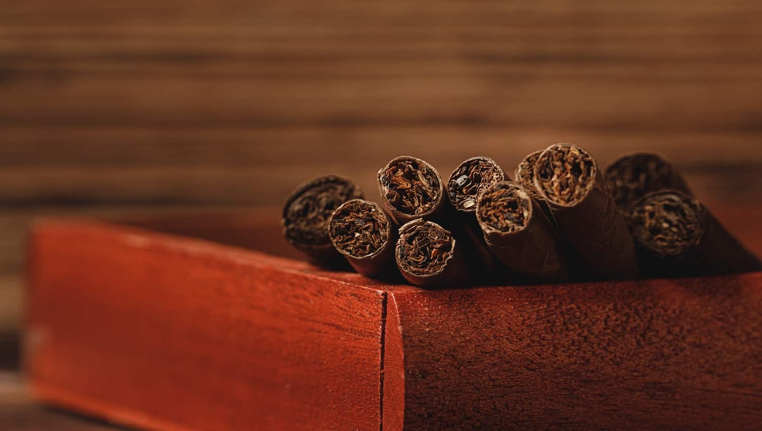 Red wooden box with new rolled cigars on wooden table close up