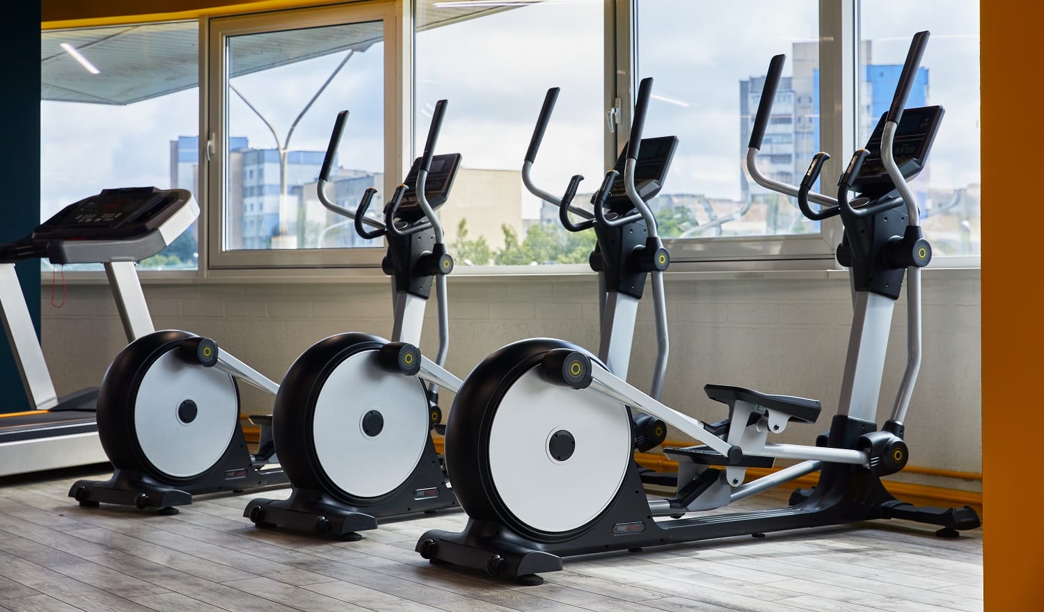 Elliptical trainers standing in a row, gym with large windows, view of the whole city