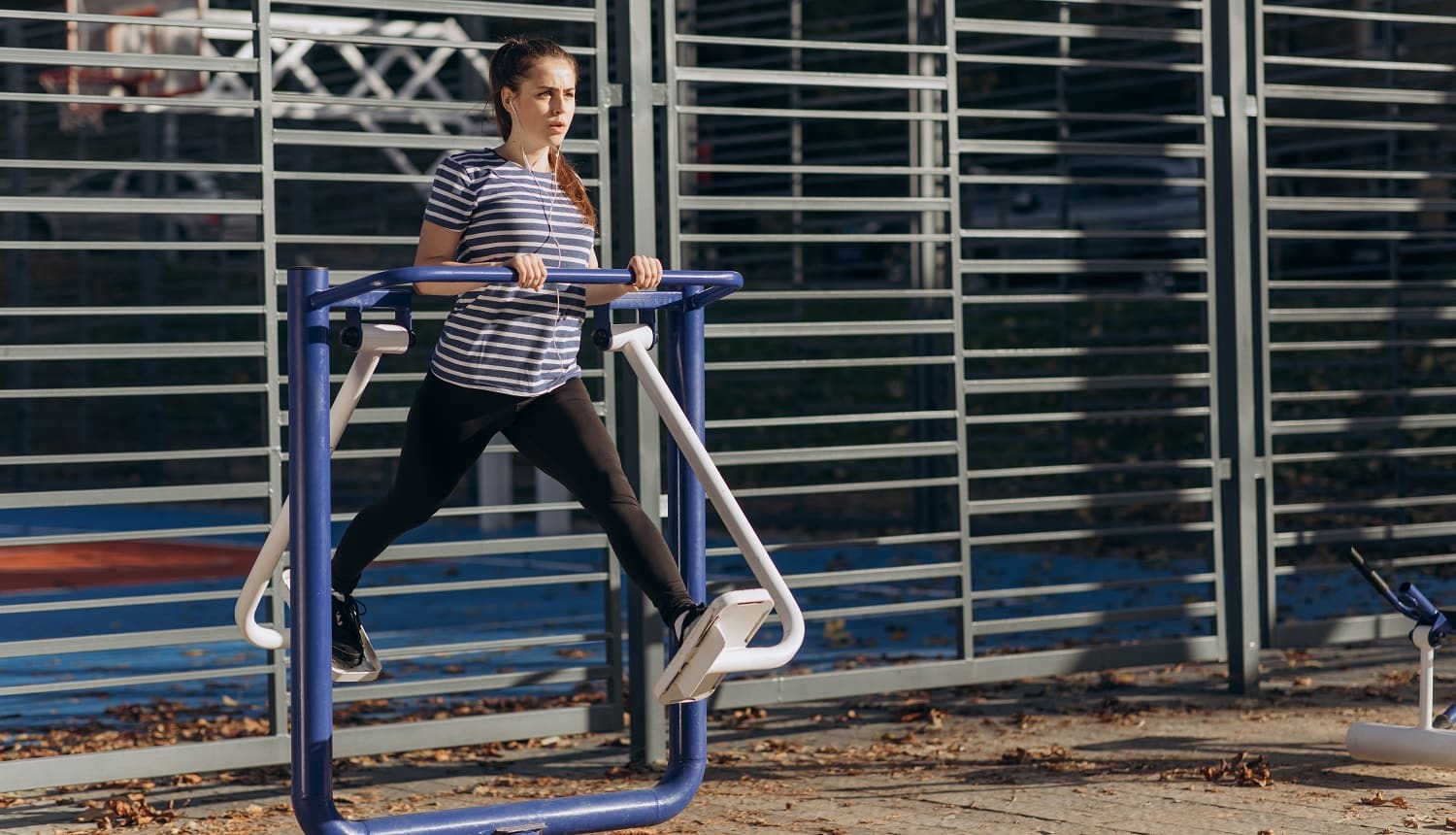 Young sportive woman do walking exercises at outdoor gym, using cross trainer machine. Sunny morning time, girl perform daily fitness workout. Concept of losing weight with exercise for health