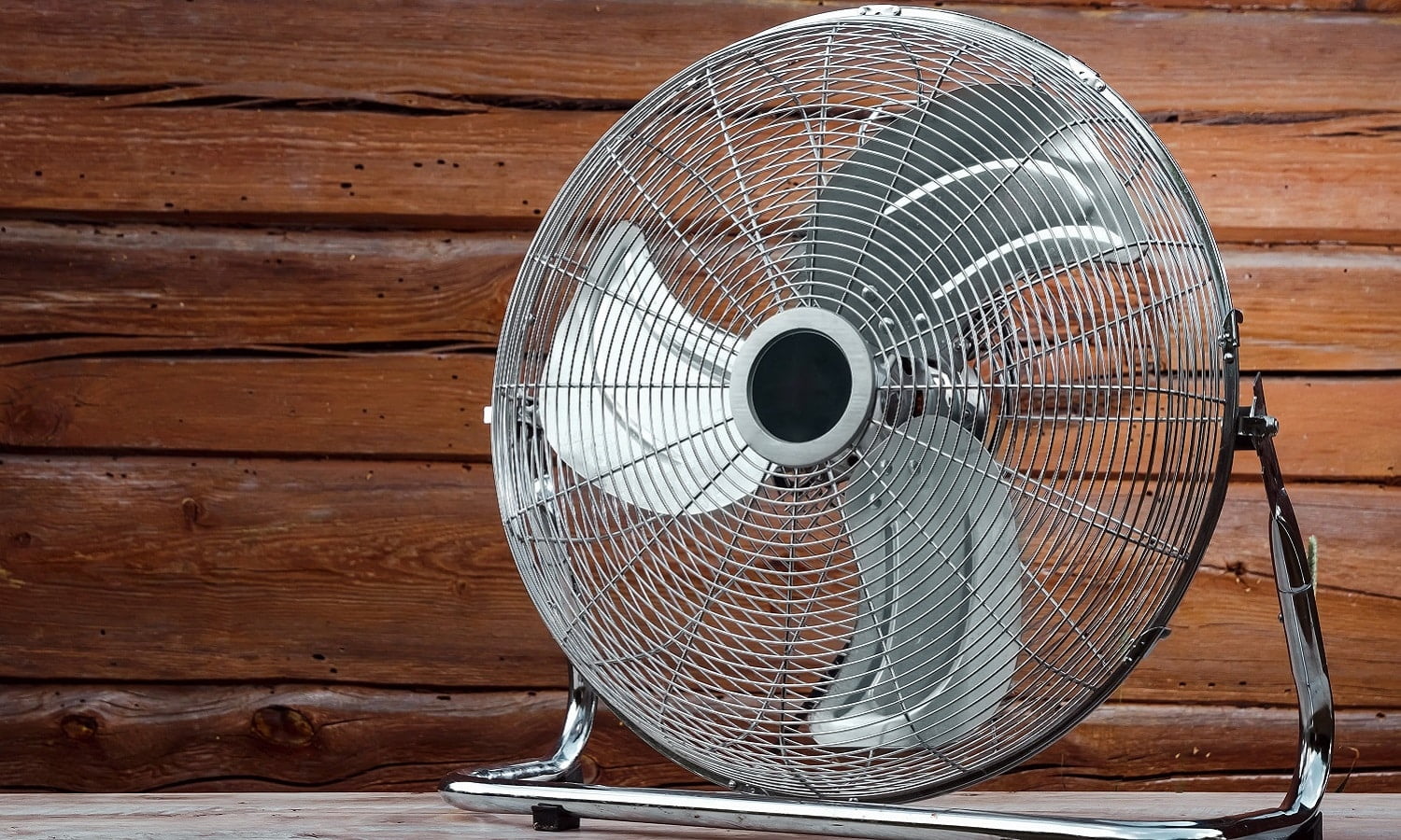 Large tabletop ventilator on the table against the background of a wooden wall. The concept of heat, hot weather, air conditioning.
